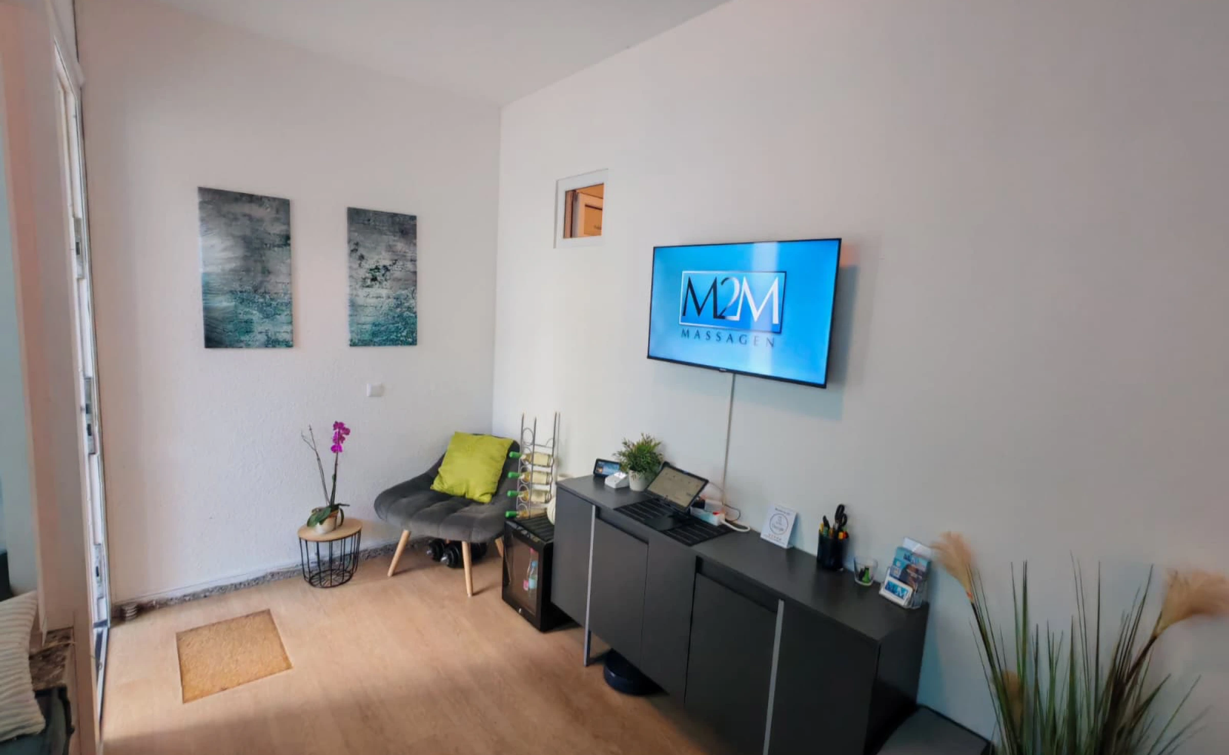 Empfangsbereich Men2Men Massage Schöneberg mit M2M Massagen TV-Display, Sessel und Orchidee